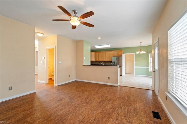 unfurnished living room featuring ceiling fan with notable chandelier, wood finished floors, and baseboards