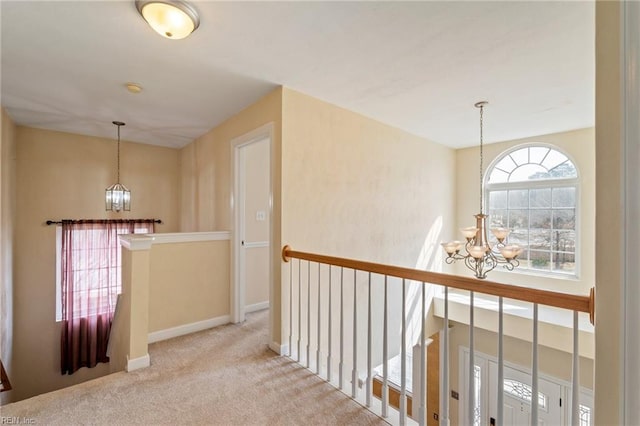 hallway with baseboards, carpet flooring, a notable chandelier, and an upstairs landing