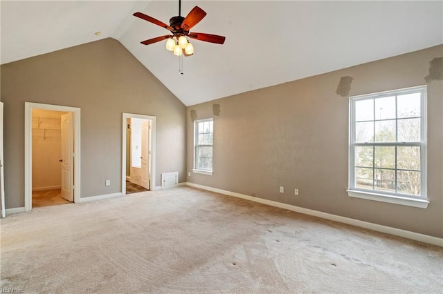 unfurnished bedroom featuring baseboards, ensuite bath, a walk in closet, carpet floors, and high vaulted ceiling