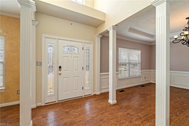 entrance foyer featuring crown molding, visible vents, a decorative wall, wood finished floors, and ornate columns