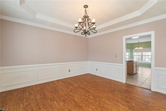 unfurnished room featuring ornamental molding, wood finished floors, a raised ceiling, and an inviting chandelier