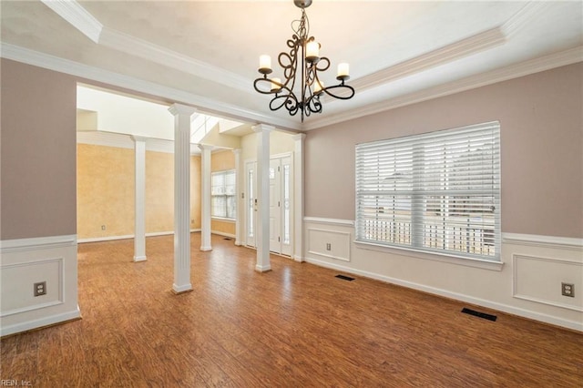 unfurnished dining area featuring decorative columns, a raised ceiling, visible vents, a decorative wall, and wood finished floors