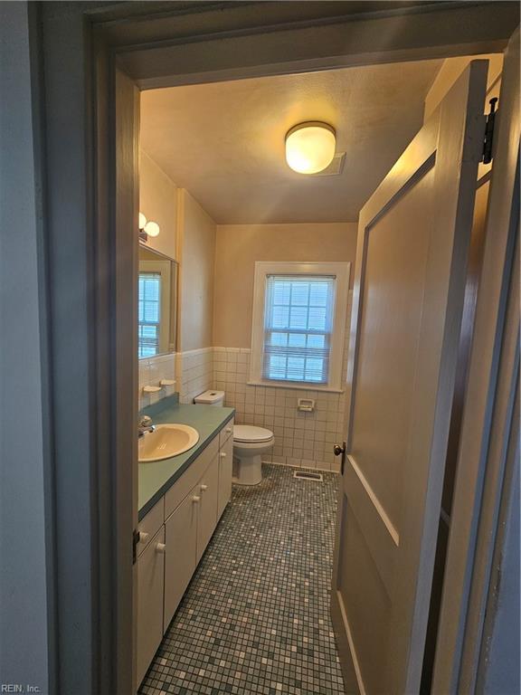 bathroom featuring tile walls, toilet, wainscoting, vanity, and tile patterned floors