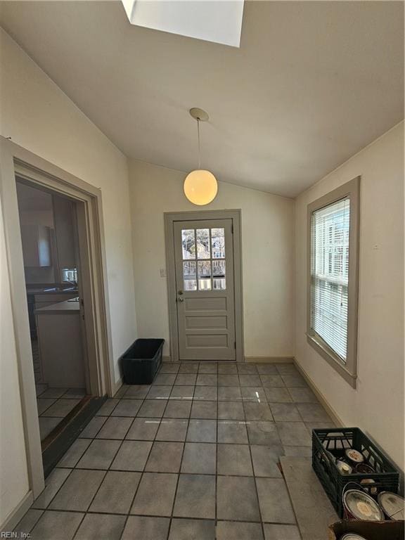 doorway featuring a healthy amount of sunlight, vaulted ceiling, baseboards, and light tile patterned flooring