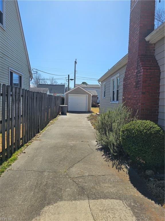 view of home's exterior with an outbuilding, a chimney, concrete driveway, fence, and a garage