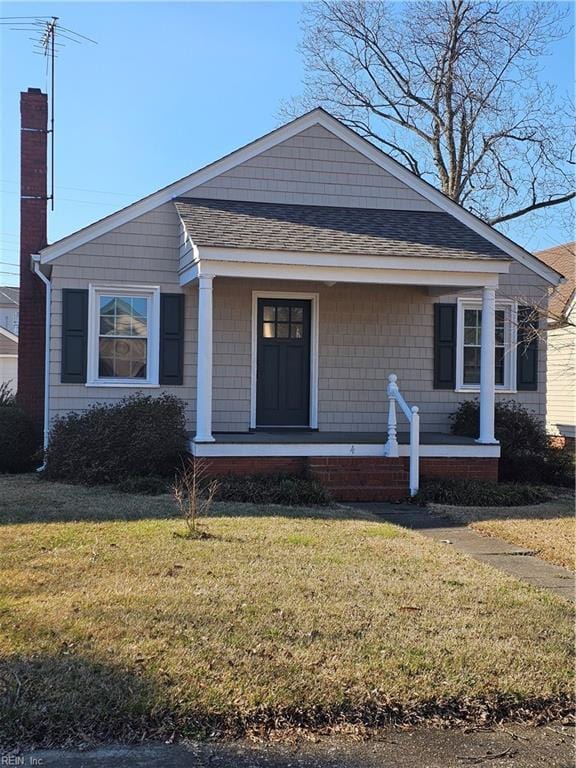 view of front facade featuring covered porch, a shingled roof, a chimney, and a front yard