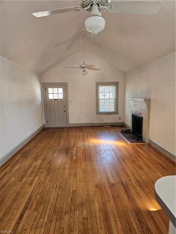 unfurnished living room with ceiling fan, a fireplace, baseboards, vaulted ceiling, and hardwood / wood-style floors