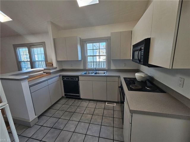 kitchen with a skylight, light tile patterned flooring, a sink, a peninsula, and black appliances