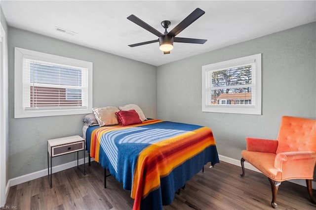 bedroom with a ceiling fan, visible vents, baseboards, and wood finished floors