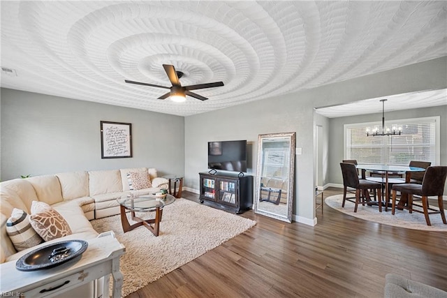 living area with baseboards, dark wood-style flooring, and ceiling fan with notable chandelier