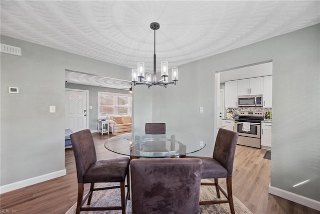 dining room with an inviting chandelier, light wood-style flooring, visible vents, and baseboards