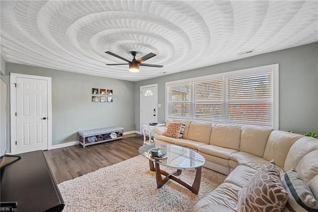 living area featuring a ceiling fan, visible vents, baseboards, and wood finished floors