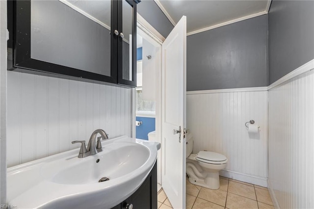 half bathroom with vanity, tile patterned floors, toilet, and wainscoting