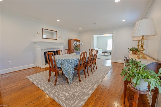 dining room featuring light wood finished floors, baseboards, a fireplace, and ornamental molding