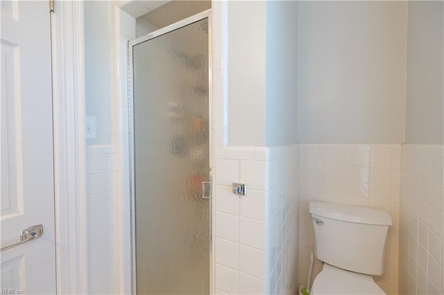 bathroom featuring toilet, a shower stall, tile walls, and wainscoting