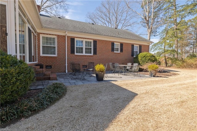 exterior space featuring crawl space, a shingled roof, a patio, and brick siding