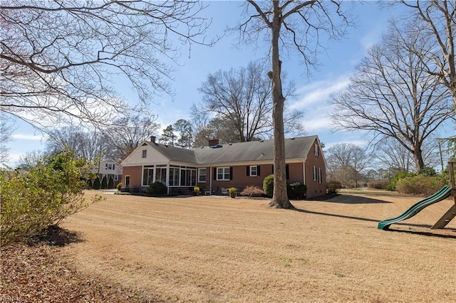 rear view of house with a yard, brick siding, a chimney, and a playground