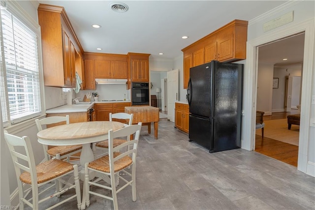 kitchen featuring visible vents, brown cabinets, under cabinet range hood, light countertops, and black appliances