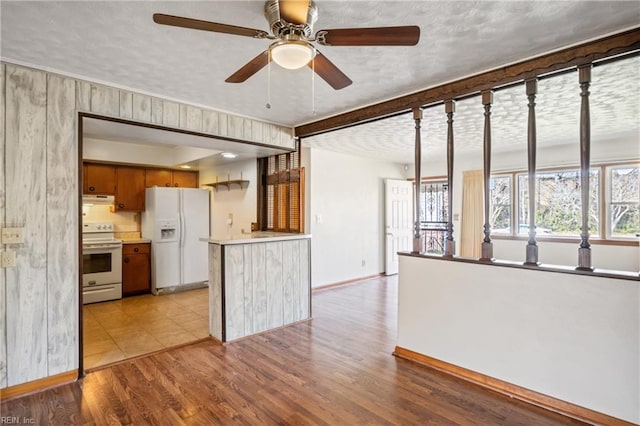 kitchen featuring light wood finished floors, under cabinet range hood, light countertops, brown cabinetry, and white appliances