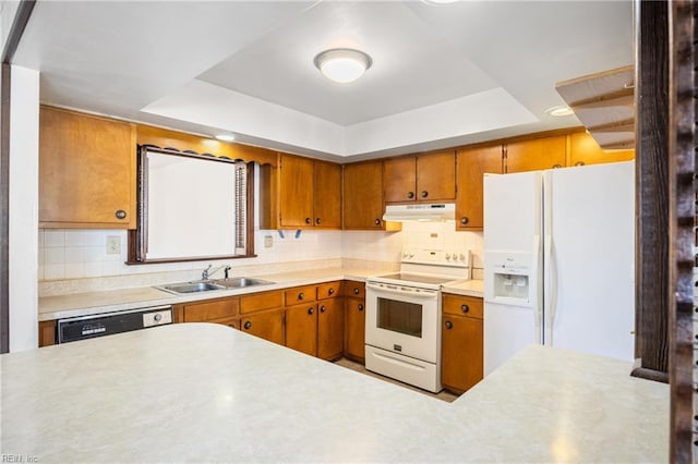 kitchen with under cabinet range hood, a tray ceiling, a sink, white appliances, and light countertops