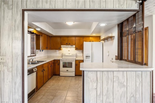 kitchen featuring white appliances, a tray ceiling, a sink, light countertops, and under cabinet range hood