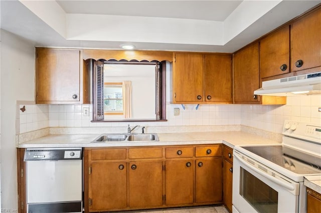 kitchen featuring under cabinet range hood, light countertops, decorative backsplash, white appliances, and a sink