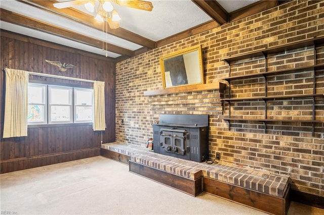 unfurnished living room with beamed ceiling, wood walls, carpet flooring, and a wood stove