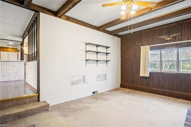 carpeted spare room with beamed ceiling, wood walls, and visible vents