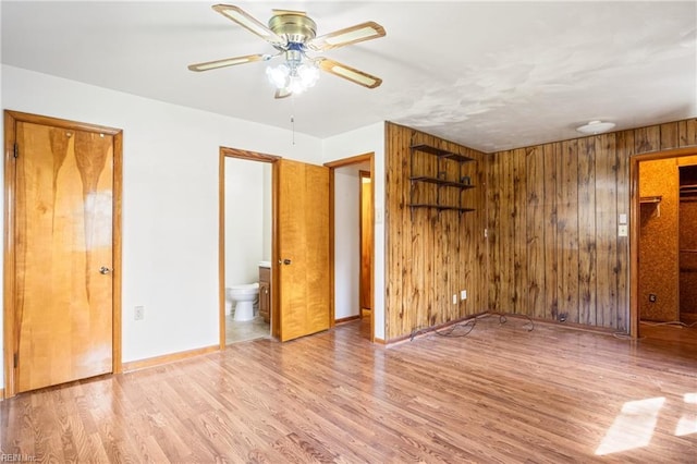 unfurnished bedroom with connected bathroom, baseboards, wood finished floors, and wood walls