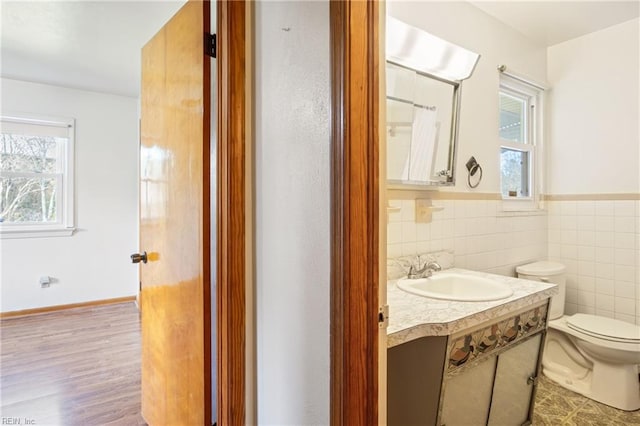 bathroom featuring a wainscoted wall, toilet, wood finished floors, tile walls, and vanity