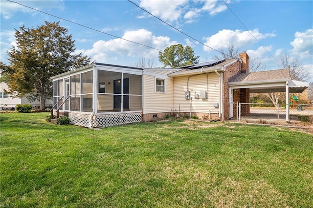 back of house featuring fence, a sunroom, a chimney, a lawn, and roof mounted solar panels