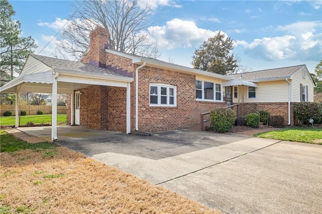 single story home with brick siding, an attached carport, a chimney, and fence