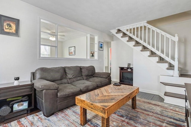 living area with a ceiling fan, baseboards, stairway, and wood finished floors