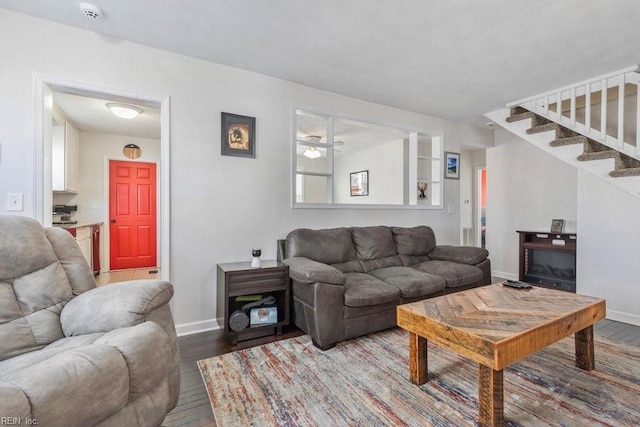 living area featuring a fireplace, stairway, baseboards, and wood finished floors