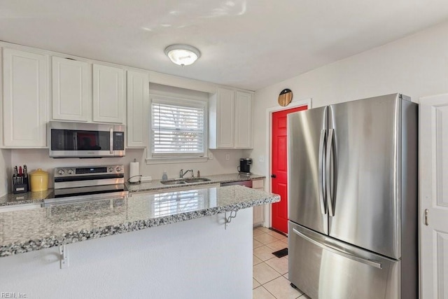 kitchen featuring a breakfast bar, light tile patterned floors, appliances with stainless steel finishes, white cabinetry, and a sink