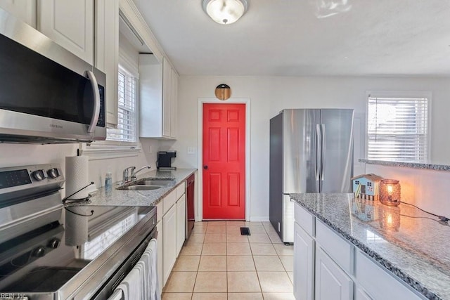 kitchen featuring light tile patterned floors, light stone counters, a sink, white cabinets, and appliances with stainless steel finishes