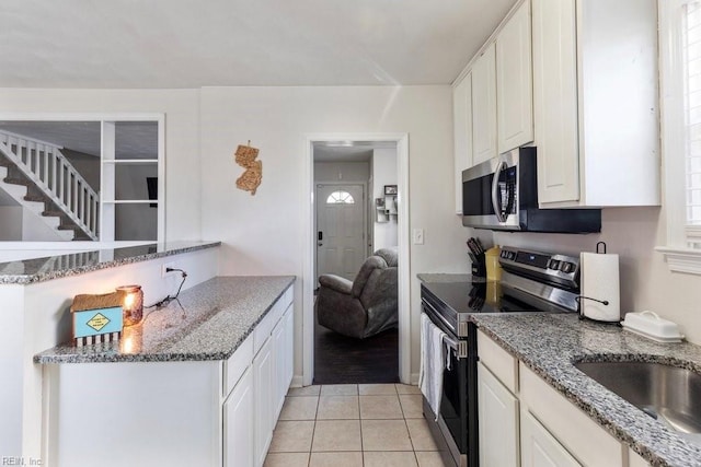 kitchen with stone countertops, white cabinets, appliances with stainless steel finishes, a peninsula, and light tile patterned flooring