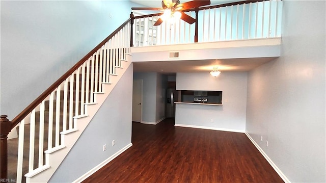 unfurnished living room featuring visible vents, a towering ceiling, a ceiling fan, wood finished floors, and baseboards