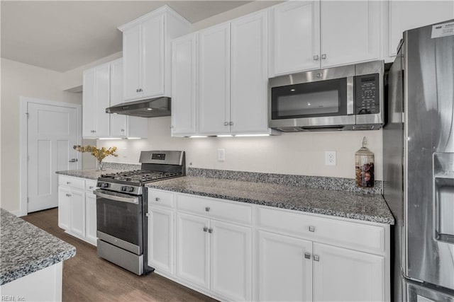 kitchen featuring under cabinet range hood, stainless steel appliances, white cabinets, dark wood-style floors, and dark stone countertops