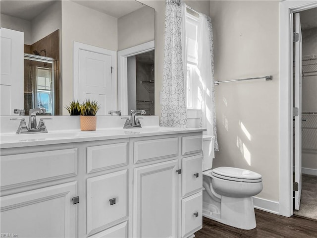 bathroom with double vanity, toilet, a sink, a shower stall, and wood finished floors