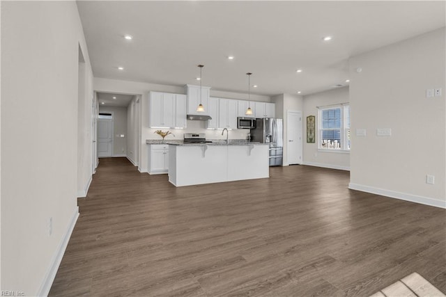 kitchen featuring a breakfast bar, dark wood-style flooring, a center island with sink, appliances with stainless steel finishes, and white cabinets