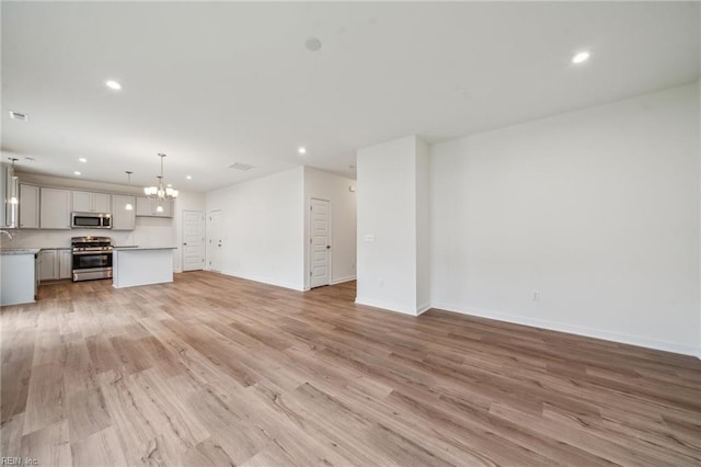 unfurnished living room featuring light wood finished floors, baseboards, a notable chandelier, a sink, and recessed lighting