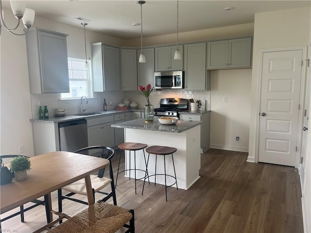 kitchen with a kitchen island, a sink, appliances with stainless steel finishes, backsplash, and dark wood-style floors