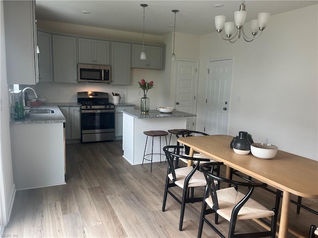 kitchen featuring stainless steel appliances, a kitchen island, a sink, light stone countertops, and light wood finished floors