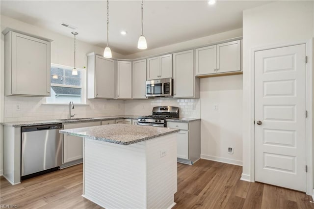 kitchen with light stone counters, light wood finished floors, visible vents, appliances with stainless steel finishes, and a sink