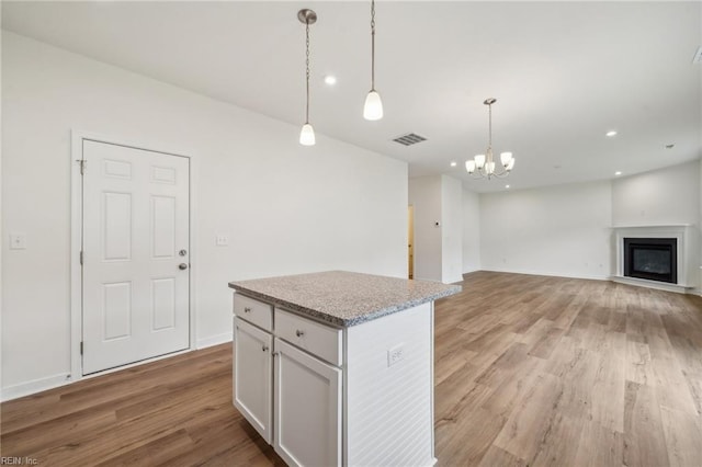 kitchen with visible vents, a glass covered fireplace, a kitchen island, hanging light fixtures, and light wood-type flooring