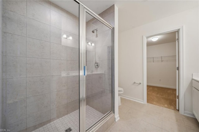 bathroom with toilet, a shower stall, baseboards, and a walk in closet