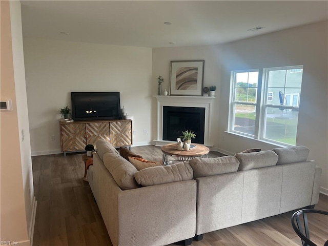 living room with a fireplace with raised hearth, wood finished floors, visible vents, and baseboards