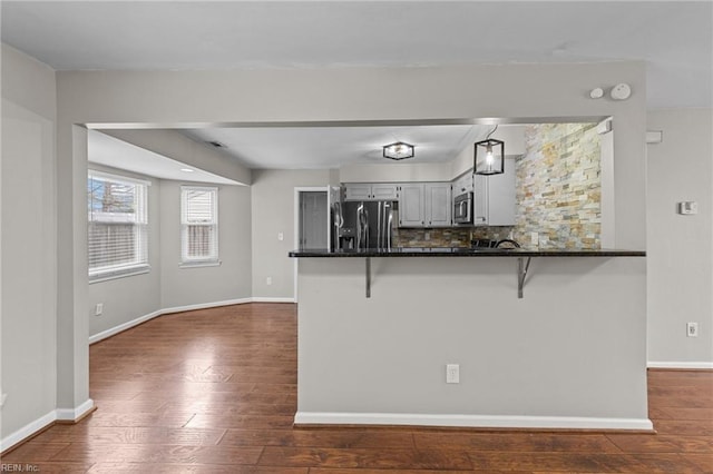 kitchen with baseboards, dark wood finished floors, stainless steel appliances, a kitchen breakfast bar, and tasteful backsplash