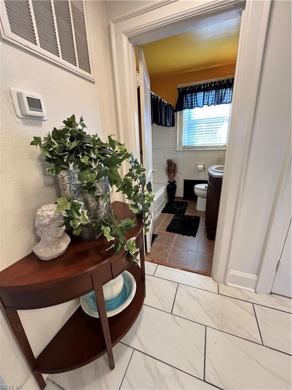 bathroom featuring toilet, marble finish floor, visible vents, and tile walls